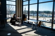 Two students sit inside at a table on a sunny day at Kent State University