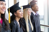 Three women and one man in graduation gowns wait for their names to be called.