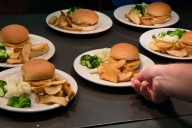 A hand reaches for a plate of food with a chicken burger, fries and vegetables