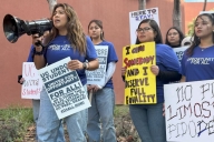 A group of undocumented students hold protest signs. One yells into a bullhorn.