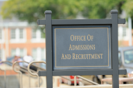A black sign on a university campus that reads "Office of Admissions and Recruitment."