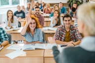 Group of happy students raising their hands to answer the professor's question in the classroom