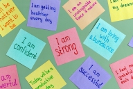 A green background decorated with colorful sticky notes featuring affirmations such as "I am confident" "I am strong" "I am living with abundance"