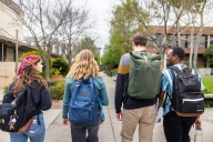 Four college students from behind walking on campus with backpacks