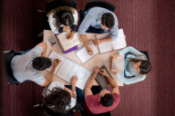 An overhead view of a group of six students studying together, their books and notebooks open, around a small, cozy table.