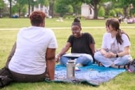 Three students sit outside on a blanket on the University of Alabama's campus