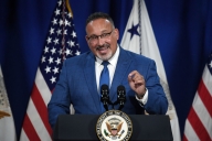 A man in a blue suit and tie at a podium in front of American flags