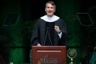 A photograph of Virginia governor Glenn Youngkin, in academic robes, speaking at a lectern with George Mason written on it.