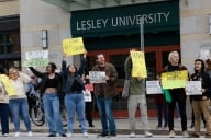 A photo of protestors holding signs objecting to job cuts at Lesley University.