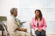 Older minority woman sits in classroom talking with younger minority woman 