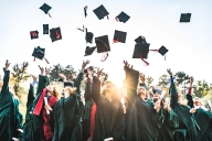 Students in graduation gowns throw their caps into the air. 