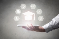 A hand holds a large phone and a digital graduation cap looms above the phone. Surrounding the digital cap are hexagons with various icons, including a light bulb and “ABC.”