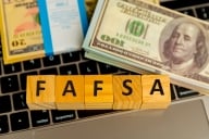 Wooden blocks spell out “FAFSA” atop a computer keyboard, next to two stacks of cash money.