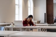 A young woman concentrating as she writes at a table in an academic setting.