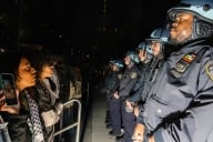 Two pro-Palestinian protestors at New York University stand face-to-face with a line of New York Police Department officers.