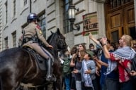 A police officer mounted on a horse, faces a group of protesting students, one holding a sign that reads “Free Palestine”.