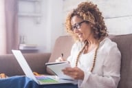 Bright window light rests on an attractive caucasian woman of middle age happily working with a laptop and notebook