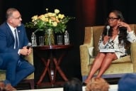 Miguel Cardona and New York Times reporter Erica Green sit in green chairs. Green is wearing a newsprint dress.