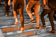 Students’ walk up a staircase with only their legs showing over the words “enrollment on the rise” on the stair risers.