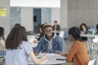 A multi-ethnic group of students sit at a table in a common space at college