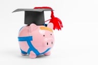 A piggy bank that has been broken and taped back together wears a small graduation mortar board