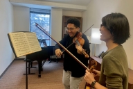 A student plays violin while smiling and looking at sheet music. 