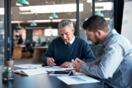 Male professor and student sit together at a table working on a paper