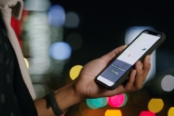 Cropped shot of a woman using a smartphone to order a cab in the city at night