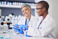 Older scientist helping younger scientist. Both are women.