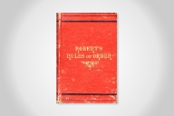 An aged copy of the original Robert's Rules of Order. The cover is red with gold writing.