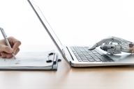 Human hand writing in script while a robot hand types on a laptop