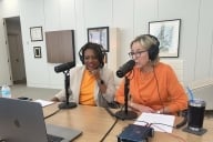Amber Williams and Donde Plowman sit next to each other, wearing University of Tennessee orange, with microphones at the table in preparation for a podcast interview.