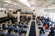 A group of faculty and inmates sit in a large room while Goucher College president Kent Devereaux speaks