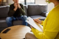 An over-the-shoulder photo of a female therapist meeting with a young male client. Neither person's face is visible.