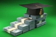 Stacks of U.S. dollars of different heights are lined up to create the impression of an ascending staircase; a graduation cap with tassel sits on the top level.