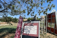 A maroon welcome sign and a campus directory with a map are heavily leaning, as in disrepair.