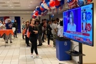 Students at Gallaudet University stand in a room next to a TV screen that shows Georgia as too early to call