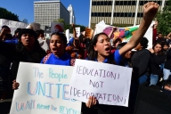 Two young people yell while holding signs, one raising a fist. A sign reads "education not deportation."