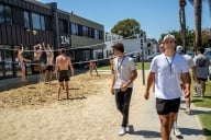 A group of students play volleyball outside of the Sigma Nu fraternity house while others walk on the sidewalk