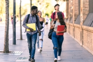 Group of students of different ethnicities walking in the street with school books in summer
