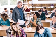 A professor speaks to an engaged student in a classroom full of students.