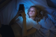Young blonde woman in bed with mobile phone.