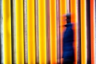 A blurred image of a person positioned toward the center-right of the frame, against a bright orange and yellow background.