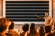 A photo illustration of a professor pointing to a whiteboard where all the text is redacted.