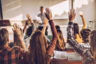 A rear view of a group of students in a lecture hall, raising their hands.