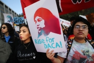 A student in a crowd holds up a sign that reads "Rise for DACA!"