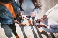 A multiethnic friend group shares things from social media with each other on their various mobile devices. View from above looking down at the phones.