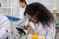 Young scientist with protective eyewear looking through a microscope in laboratory for medical and biological research.