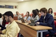 Several rows of students in a college classroom chat and look around while waiting for their class to start.