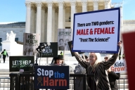 A blonde congresswoman holds up a sign that says there are "two genders, male and female," and "trust the science."
